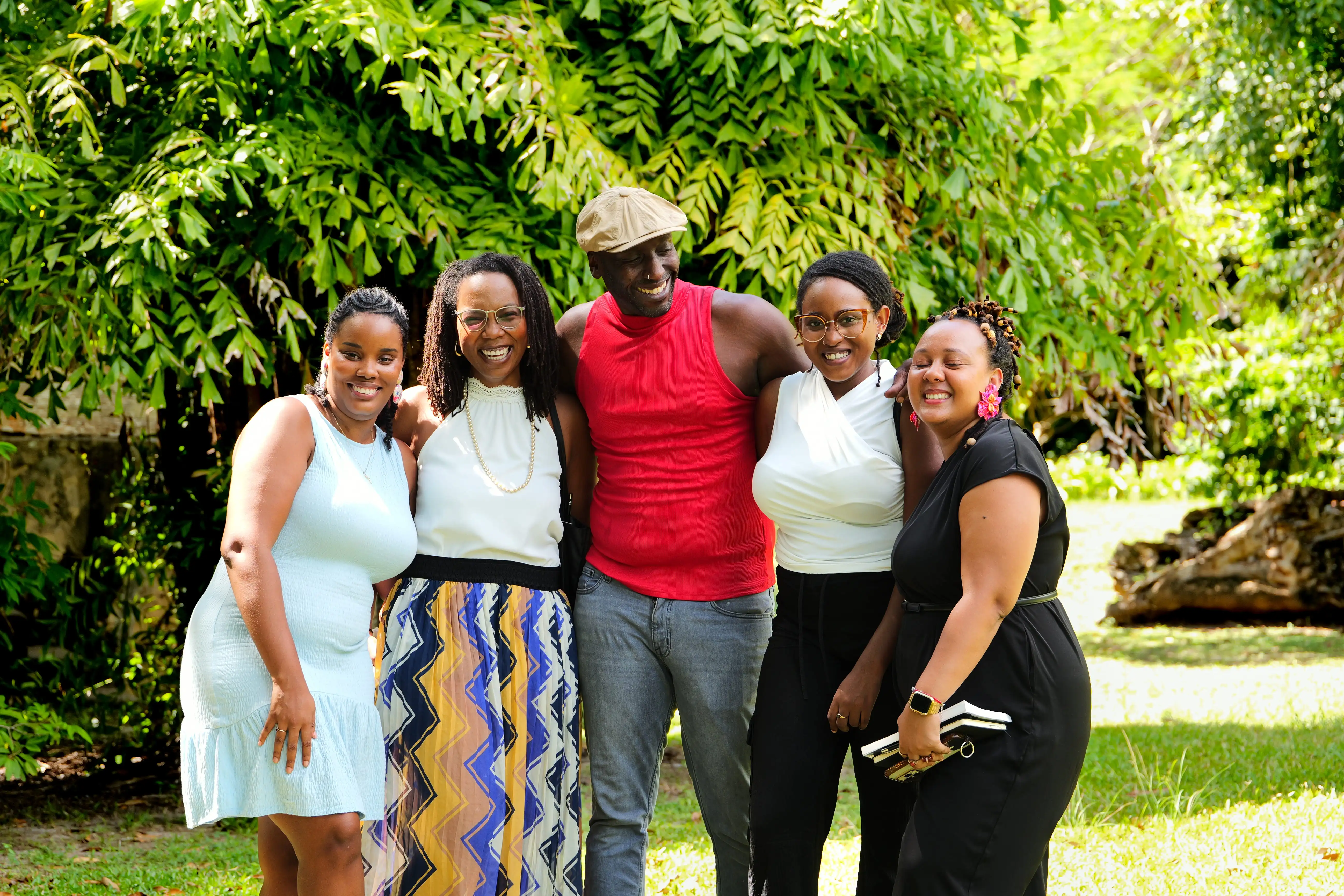 Five Listwa Collective team members standing arm in arm outdoors, smiling in front of lush greenery